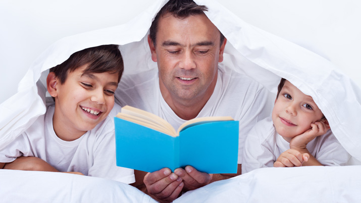 Un padre leyendo un cuento a sus dos hijos bajo una sábana